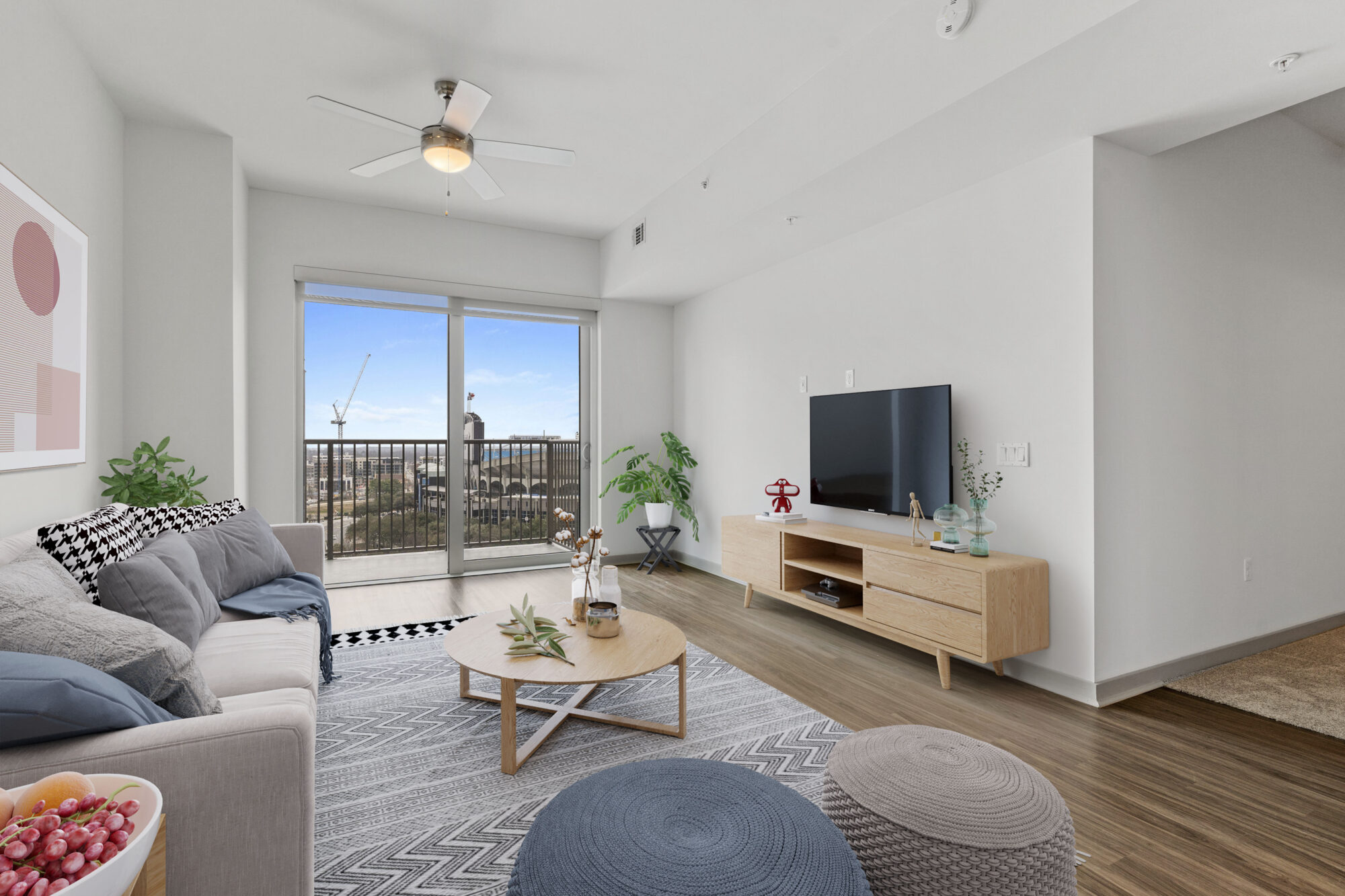 A picture of a fully furnished living room with a couch and television showing a balcony view of a blue sky